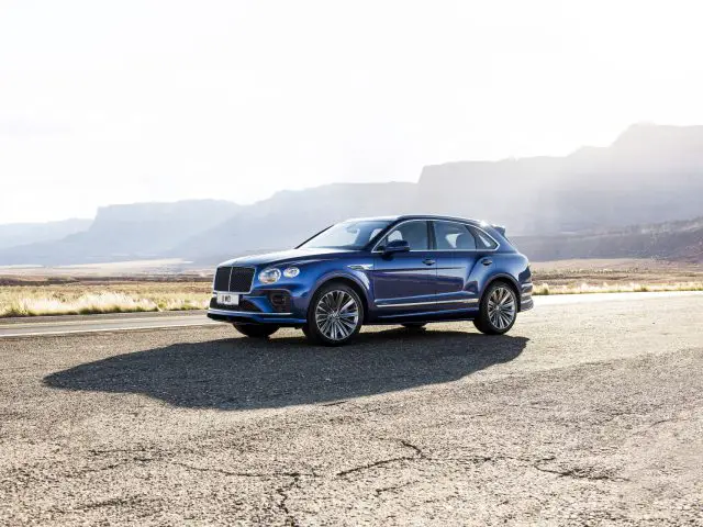 Een blauwe Bentley Bentayga Speed geparkeerd op een weg met een heldere hemel en een bergachtige horizon op de achtergrond.