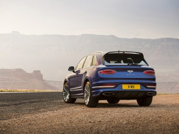 Een blauwe Bentley Bentayga Speed geparkeerd op een weg met een woestijnkloof op de achtergrond tijdens zonsondergang.
