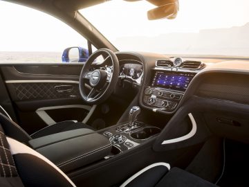 Binnenaanzicht van een Bentley Bentayga Speed met een modern dashboard, leren stoelen en uitzicht op een zonsondergang door de voorruit.