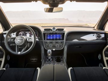 Binnenaanzicht van een Bentley Bentayga Speed met een modern dashboard, lederen stoelen en een gedetailleerd stuur, met een schilderachtig woestijnlandschap zichtbaar door de voorruit.
