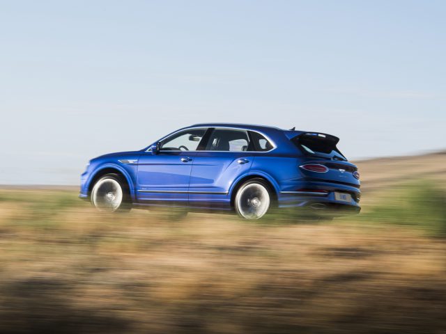 Bentley Bentayga Snelheid die met hoge snelheid over een onverharde weg reist in een landelijke omgeving, met bewegingsonscherpte op de achtergrond.