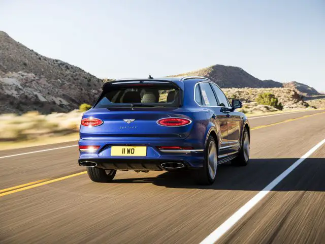 Een blauwe Bentley Bentayga Speed SUV die op een snelweg door een woestijnlandschap rijdt.