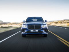 Een blauwe Bentley Bentayga Speed die te hard rijdt op een open snelweg met een heldere lucht en een woestijnlandschap op de achtergrond.