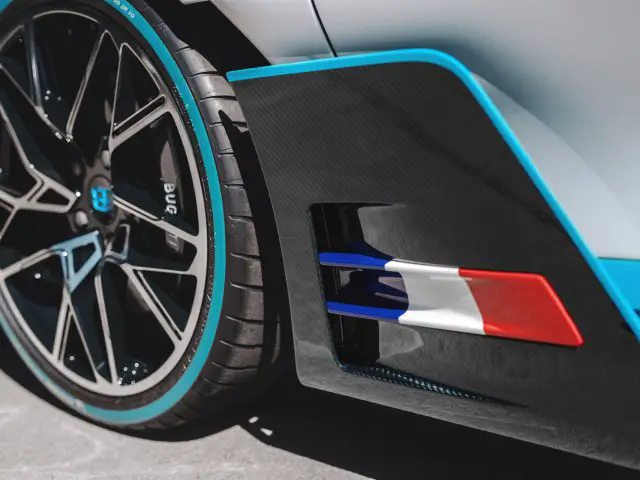 Close-up van het achterwiel en het spatbord van een Bugatti Divo, met blauwe en rode strepen op een witte achtergrond met details van koolstofvezel.