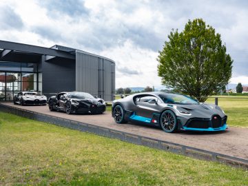 Luxe sportwagens, waaronder een Bugatti Divo, geparkeerd buiten een modern gebouw, met de nadruk op een prominente blauw-zwarte auto op de voorgrond.