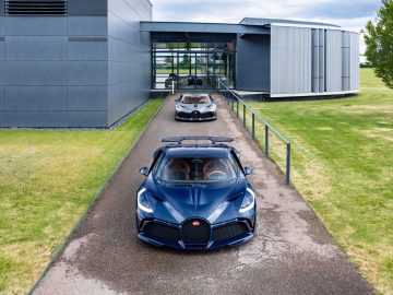 Twee Bugatti Divo-sportwagens, één donkerblauw en één zilverkleurig, geparkeerd voor een modern gebouw op een bewolkte dag.
