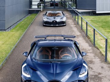 Luchtfoto van twee Bugatti Divo-sportwagens, een blauwe en een bruine, geparkeerd voor een modern gebouw met een glazen ingang.