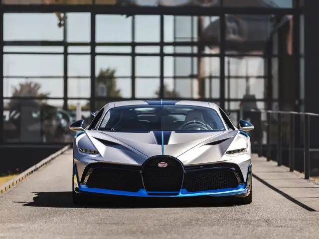 Een Bugatti Divo geparkeerd voor een modern glazen gebouw op een zonnige dag.
