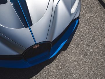 Close-up van de voorkant van een grijs-blauwe sportwagen, waarbij het strakke ontwerp en het Bugatti Divo-logo op de grille benadrukt worden.