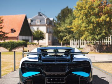 Achteraanzicht van een blauwe en zwarte Bugatti Divo geparkeerd op een weg met huizen en bomen op de achtergrond op een zonnige dag.