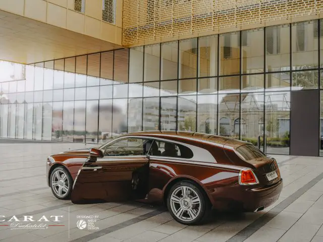 Luxe Rolls-Royce Silver Spectre Shooting Brake geparkeerd voor een modern gebouw met grote glazen ramen en gouden panelen.