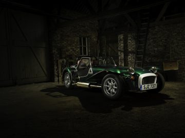 Een vintage groene Caterham Super Seven 1600 sportwagen geparkeerd in een slecht verlichte, rustieke schuur.
