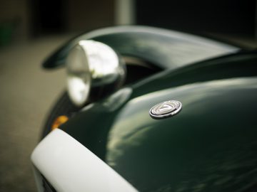 Close-up van een groene Caterham Super Seven 1600-sportwagen, gericht op de koplamp en motorkap, met het merklogo zichtbaar.