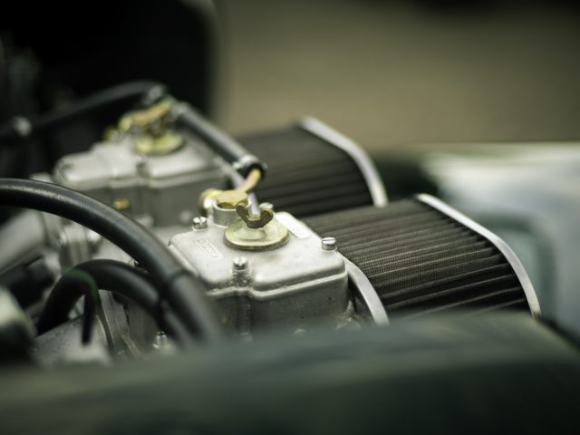 Close-up van een Caterham Super Seven 1600-motor met gedetailleerde onderdelen, waaronder luchtfilters en metalen componenten, met een geringe scherptediepte.