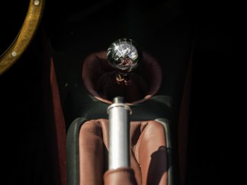 Uitzicht van achter een kanonloop die rechtstreeks naar een kristallen bol wijst die door een persoon wordt vastgehouden, waarbij de achtergrond het interieur van een Caterham Super Seven 1600 suggereert.