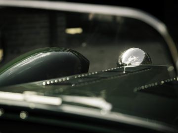 Close-up van de glanzende groene motorkap van een Caterham Super Seven 1600 met een chromen zijspiegel die zonlicht reflecteert.