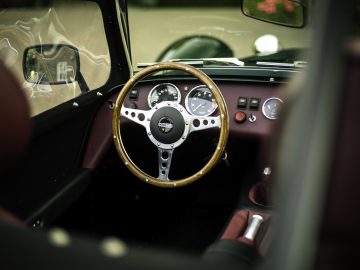 Uitzicht door een open autodeur met het stuur en het dashboard van een Caterham Super Seven 1600 met een houten stuur.