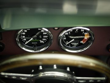 Close-up van een Caterham Super Seven 1600 dashboard met snelheidsmeter en toerenteller met een zichtbaar houten stuurwiel.