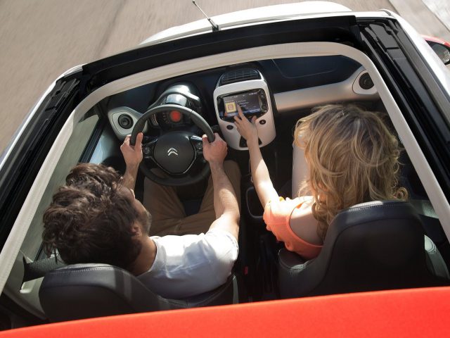 Bovenaanzicht van een echtpaar in een Citroën C1 cabriolet, de vrouw navigeert met een GPS-apparaat en de man rijdt.