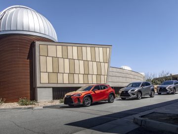 Rode en grijze Lexus SUV's geparkeerd buiten moderne observatoriumgebouwen onder een helderblauwe hemel.