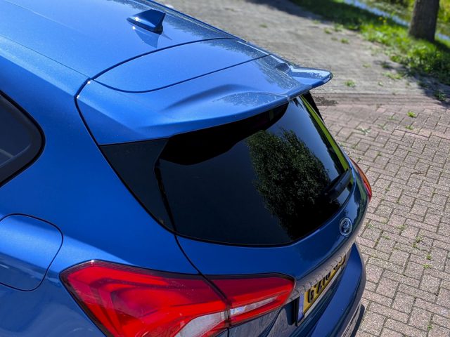 Close-up van de achterkant van een blauwe Ford Focus ST met de focus op de spoiler en de achterlichten, buiten geparkeerd op een zonnige dag.