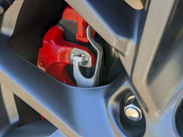 Close-up van de remklauw en schijf van een rode auto, zichtbaar door een zwarte lichtmetalen velg op een Ford Focus ST, met de nadruk op het Brembo-merk.