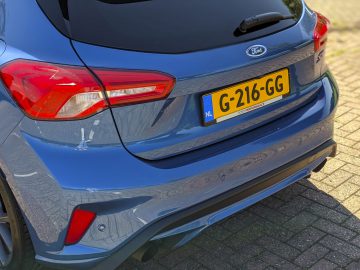 Achteraanzicht van een blauwe Ford Focus ST met zichtbaar Nederlands kenteken, geparkeerd op een zonnige dag.