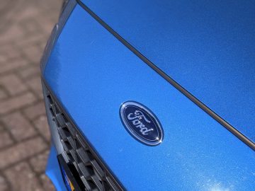 Close-up van de motorkap en het embleem van een blauwe Ford Focus ST-auto met een focus op textuur- en kleurdetails.