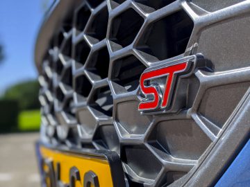Close-up van de grille van een Ford-auto met een 'ST'-badge, met de nadruk op het gestructureerde ontwerp en het levendige rode embleem.