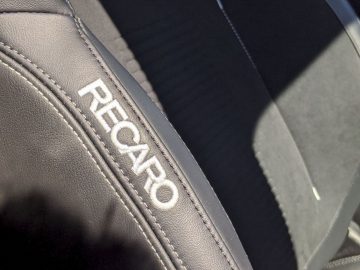 Close-up van een zwart Recaro-autostoeltje van een Ford Focus ST met het logo in reliëf op leer, waarbij zonlicht de textuur benadrukt.