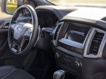 Binnenaanzicht van een Ford Ranger met stuur en dashboard met digitaal beeldscherm, gemerkt met "raptor".