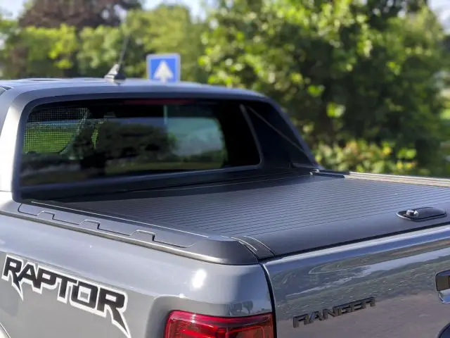 Close-up van het achterste gedeelte van een grijze Ford Ranger pick-up, met de nadruk op het logo, gelegen in een zonnige buitenomgeving.