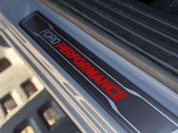 Close-up van een 'Ford Ranger performance'-logo op de dorpelbeschermer van een auto tegen een gestructureerde achtergrond.