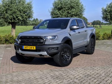Een zilveren Ford Ranger geparkeerd op een bakstenen stoep met groen gras en bomen op de achtergrond op een zonnige dag.