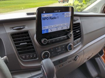 Autodashboard van een Ford Transit Custom, met een digitaal radiodisplay afgestemd op npo radio 1, omgeven door ventilatieopeningen en bedieningsknoppen.