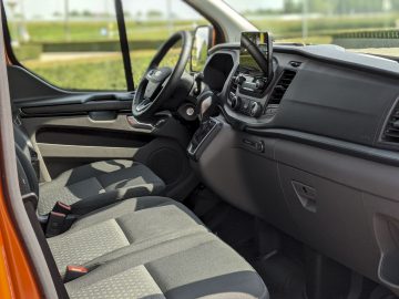 Binnenaanzicht van een Ford Transit Custom met de bestuurdersstoel, het stuur, het dashboard en de open voordeur.