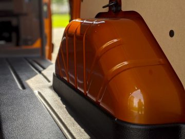 Oranje rolstoelhelling opgevouwen in een Ford Transit Custom-bus, verlicht door zonlicht dat door het raam van het voertuig stroomt.