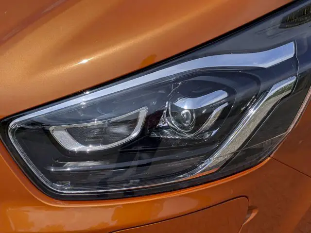 Close-up van de koplamp van een moderne Ford Transit Custom op een oranje voertuig, met een gedetailleerd ontwerp en een schoon oppervlak.