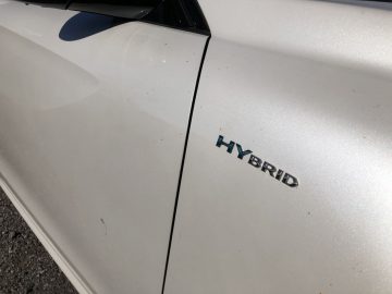 Close-up van een witte Peugeot 508 HYbrid met een "hybride" badge op het zijpaneel, met enkele vuilvlekken rondom.