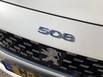 Close-up van een Peugeot 508 HYbrid-autologo en modelnummer op een wit autorooster.