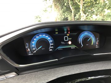 Digitaal dashboard van een Peugeot 508 HYbrid met snelheidsmeter, batterijniveau en brandstofmeter, waarbij verschillende waarschuwingslampjes branden.