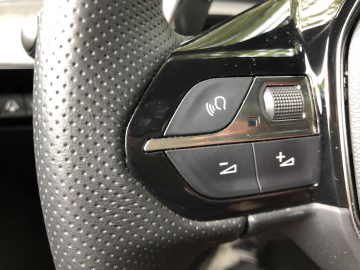 Close-up van een Peugeot 508 HYbrid-stuurwiel met audiobedieningsknoppen en een spraakopdrachtsymbool.