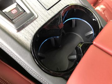 Close-up van de bekerhouder van een Peugeot 508 HYbrid met een reflecterend zwart oppervlak, omgeven door rood leer, met interieurdetails.