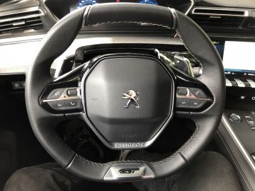Stuur van een Peugeot 508 HYbrid met bedieningselementen en het bedrijfslogo, gezien vanuit het perspectief van de bestuurdersstoel.