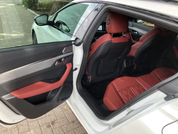 Autodeur open met interieurontwerp met roodleren stoelen, onderdeel van een witte Peugeot 508 HYbrid buitenkant geparkeerd buiten.