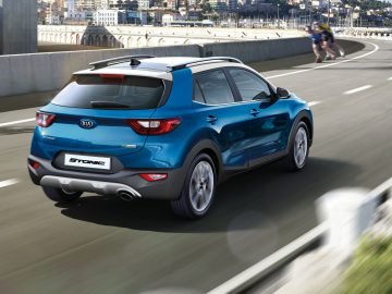 Een blauwe Kia Stonic SUV rijdt langs een kustweg met een fietser op de achtergrond.