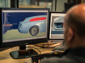 Man die computersoftware gebruikt om een Rolls-Royce Silver Spectre Shooting Brake-onderdeel te ontwerpen of analyseren, waarbij hij zich concentreert op een monitor waarop een 3D-model van een autodeur wordt weergegeven.