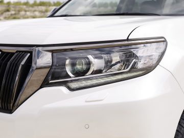 Close-up van de koplamp van een Toyota Land Cruiser en een deel van de grille, met moderne auto-ontwerpdetails.