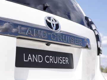 Close-up van het achterembleem van een witte Toyota Land Cruiser onder een heldere hemel.