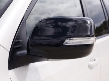 Close-up van een zwarte autozijspiegel op een witte Toyota Land Cruiser, met een geïntegreerd richtingaanwijzer.